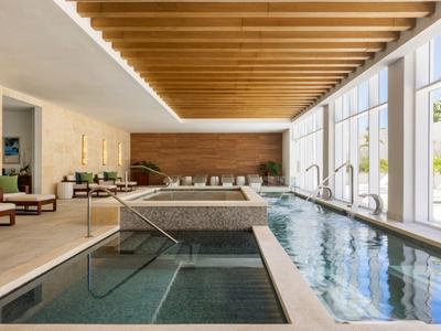 Bright indoor pool with wooden ceiling, hot tub, and lounge area next to large windows.