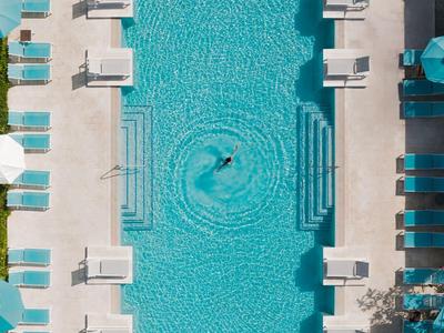 Rectangular pool with blue loungers and white umbrellas on light ground