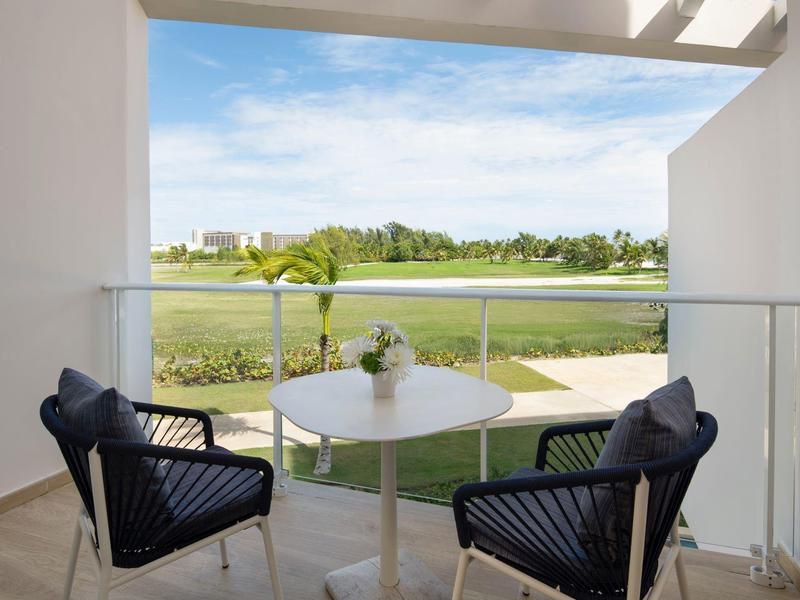 Balcony with table and chairs overlooking golf course and greenery.