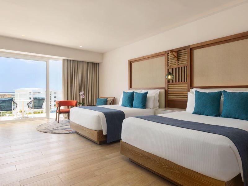 Hotel room with two beds, balcony overlooking the sea, and modern furniture.