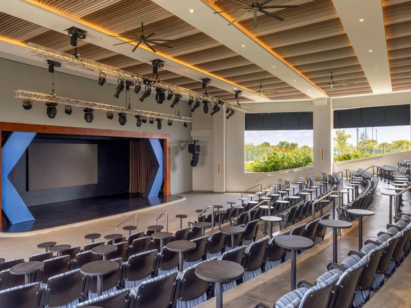 Large modern event hall with many chairs and a stage, surrounded by large windows.