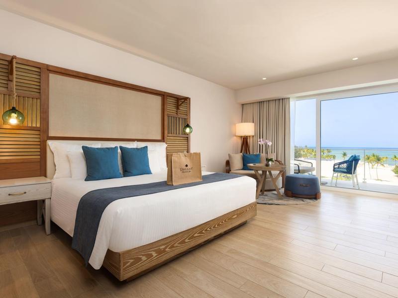 Bright hotel room with large bed, balcony, and sea view.