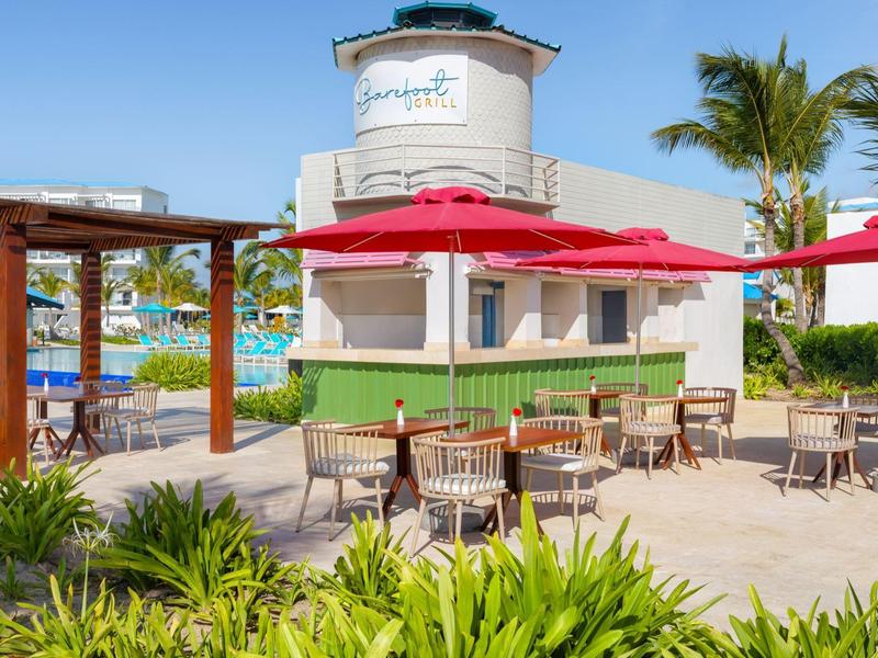 Outdoor bar area with red umbrellas and tables in a tropical setting.