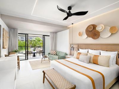 Helles Schlafzimmer mit großem Bett, Deckenventilator, grüner Couch und Balkon mit Blick ins Grüne.