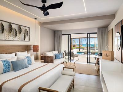 Modern eingerichtetes Hotelzimmer mit Bett, Sitzbereich und Blick auf Terrasse und Meer.