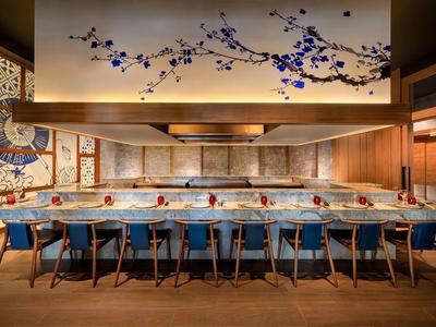 Moderner Raum mit langem Holztisch, blauen Sesseln, Wandkunst und einem Deckengemälde mit blauen Blüten.