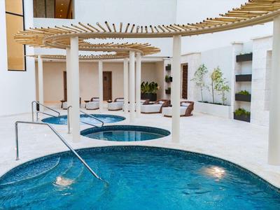 Modernes Spa mit rundem Whirlpool, hellem Ambiente und weißen Säulen unter Holzlamellen.