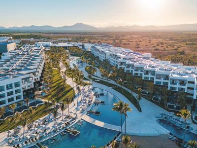 Großes Hotelresort mit mehreren Pools und weißen Gebäuden in einer sonnenbeschienenen Landschaft.