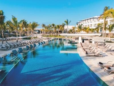 Grande piscine extérieure avec transats et palmiers dans une station balnéaire ensoleillée.