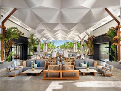 Großer, moderner Hotel-Loungebereich mit bequemen Sesseln und Palmen, hell und luftig gestaltet.