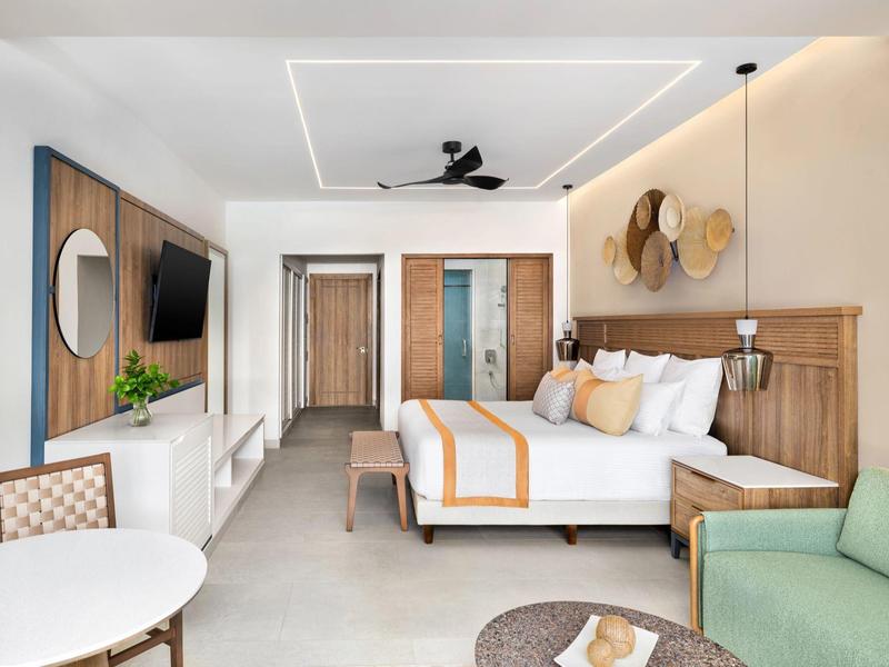 Moderne, helle Hotelzimmer mit großem Bett, TV, grünem Sofa und kleiner Sitzecke.