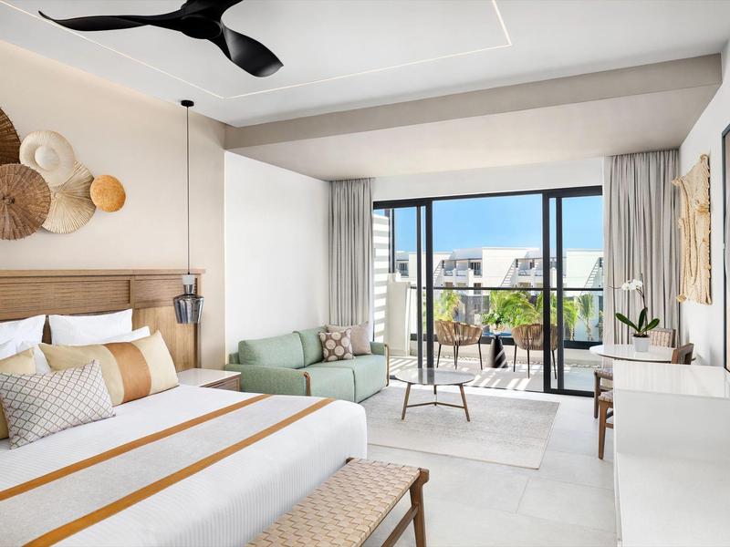 Helles, modernes Schlafzimmer mit großem Bett, Sitzbank, Sofa und Balkon mit Stadtblick.