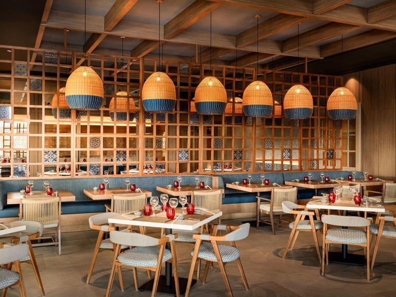 Modernes Restaurant mit Holzmöbeln, blauen Sitzpolstern und großen, hängenden Lampen aus Holz und Blau.