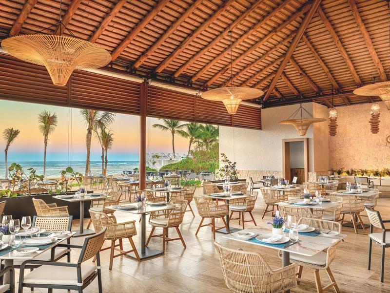 Freiluftrestaurant mit Blick auf Meer, Holzdach und modernen Möbeln in warmem Ambiente.