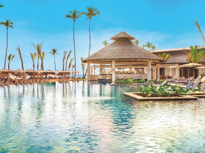 Großer Pool mit Liegestühlen und tropischen Palmen in einem Hotelresort.