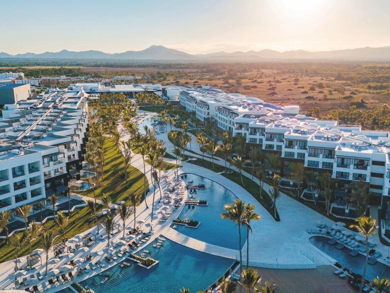 Großes Hotelresort mit mehreren Pools und weißen Gebäuden in einer sonnenbeschienenen Landschaft.