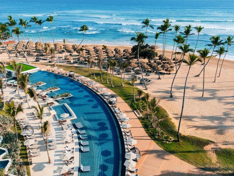 Blick auf einen Strandresort mit Pool, Palmen und Liegestühlen am Meer