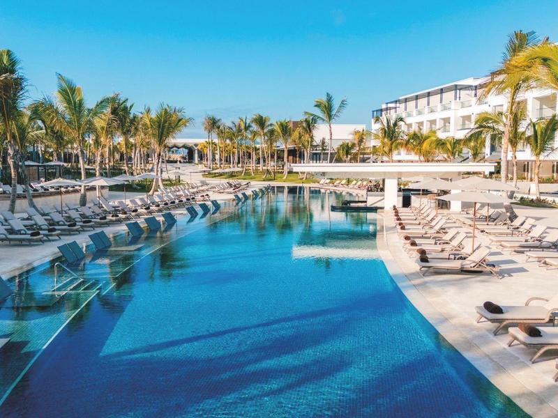 Großer Hotelpool mit Sonnenliegen und Palmen unter blauem Himmel