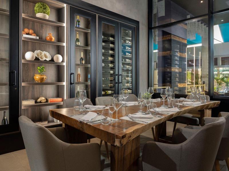 Moderner Essbereich mit Holztisch, bequemen grauen Stühlen und Glasvitrine mit Wein- und Dekorartikeln.