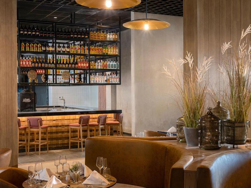 Gemütliche Bar mit Holztheke, hohen Stühlen, Regalen mit Flaschen und braunen Ledersesseln.