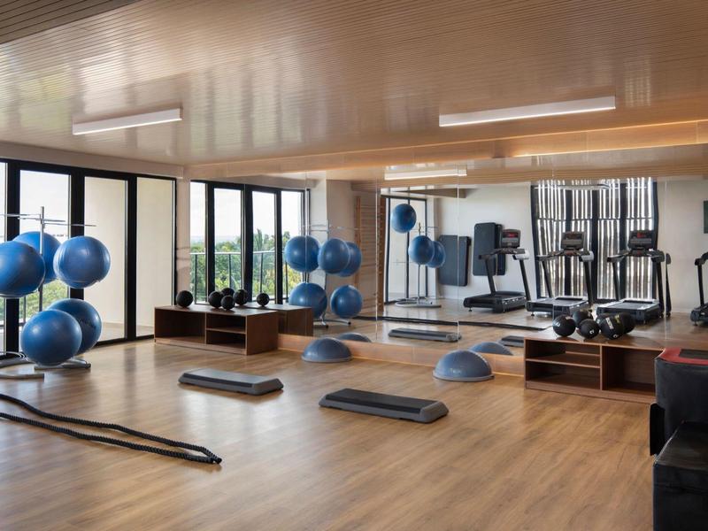 Großer, heller Fitnessraum mit Holzfußboden, Spiegelwand und verschiedenen Trainingsgeräten.