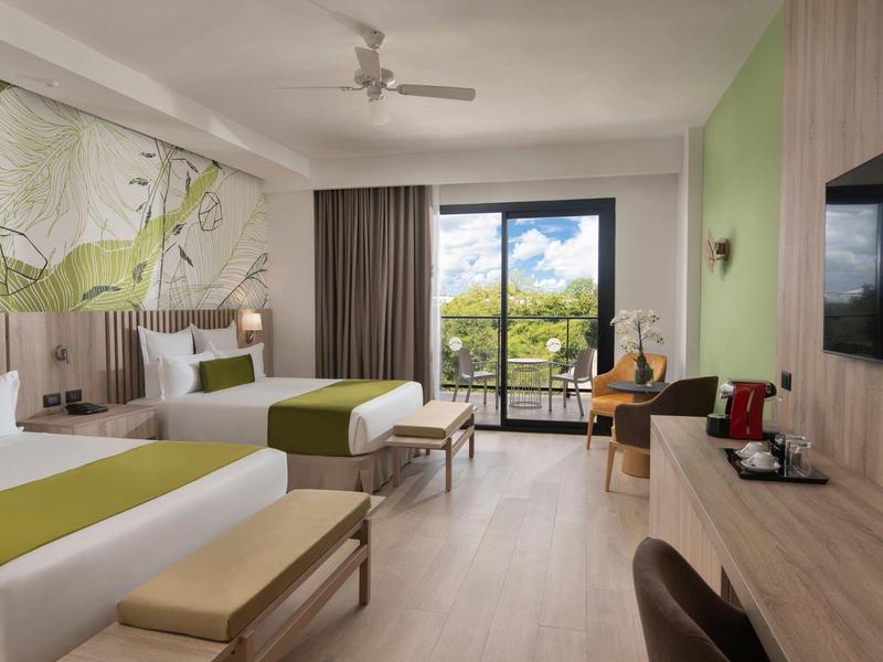 Modern eingerichtetes Hotelzimmer mit zwei Betten, Balkon, grünen Akzenten und großer Wanddekoration.