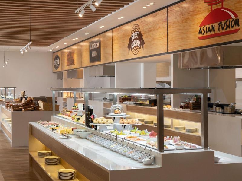 Buffet mit asiatischen Speisen, helle Holzwände, moderne Beleuchtung und übersichtliche Anordnung.