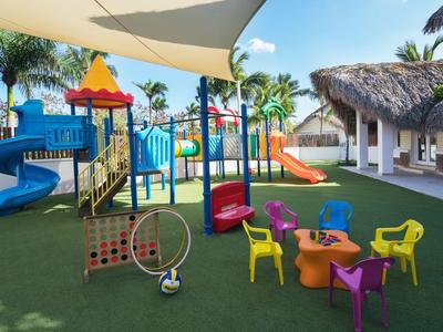 Bunter Kinderspielplatz mit Rutschen und Sitzbereich unter Sonnensegel im Hotelgarten