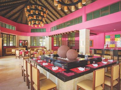 Hell gestalteter Speisesaal mit rosa Wänden, langen Tischen und Stühlen unter einer Holzbalkendecke.