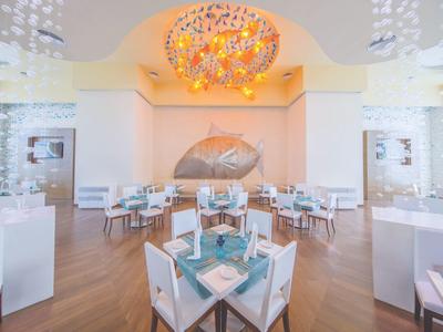 Helles Restaurant mit weißem Mobiliar, blauem Geschirr und farbenfroher Deckendekoration.