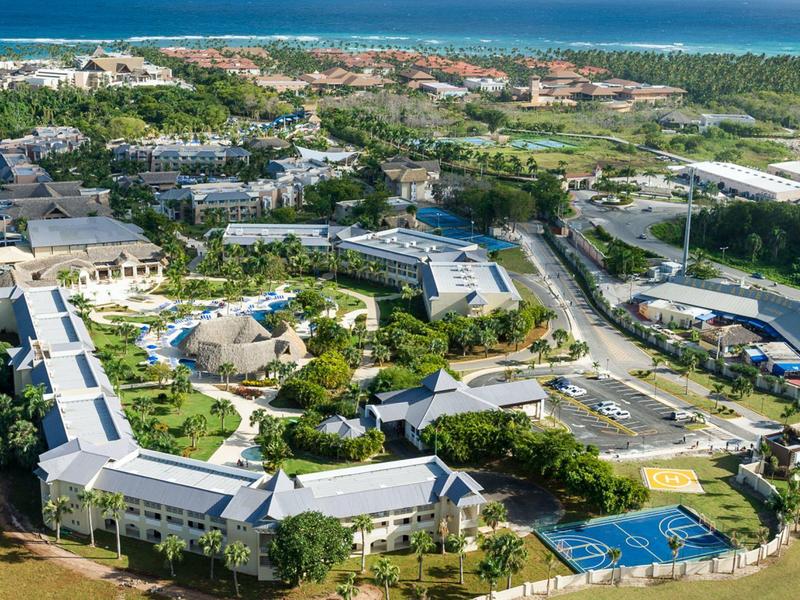 Luftaufnahme eines großen, modernen Campus mit Gebäuden, Grünflächen und Tennisplätzen am Meer.