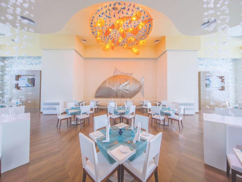 Helles Restaurant mit weißem Mobiliar, blauem Geschirr und farbenfroher Deckendekoration.