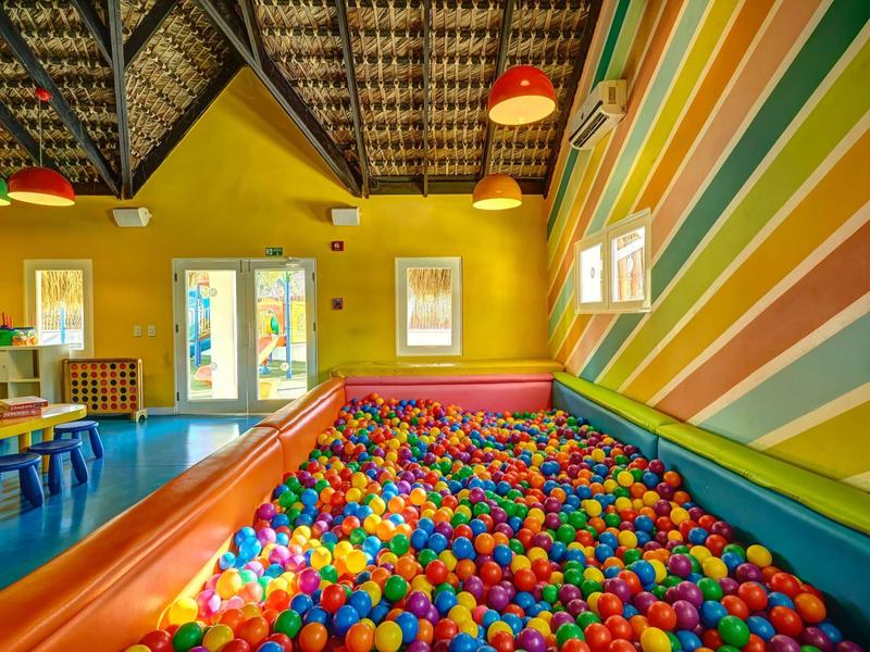 Bunter Ballpool in einem farbenfrohen Spielzimmer mit gestreiften Wänden und Decke aus Holz.