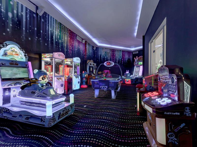 Ein bunt erleuchteter Arcade-Spielraum mit verschiedenen Spielautomaten und Neonlichtern.