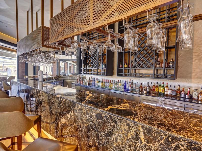 Luxusní bar s velkým mramorovým pultem a množstvím lahví alkoholu v elegantním prostředí.