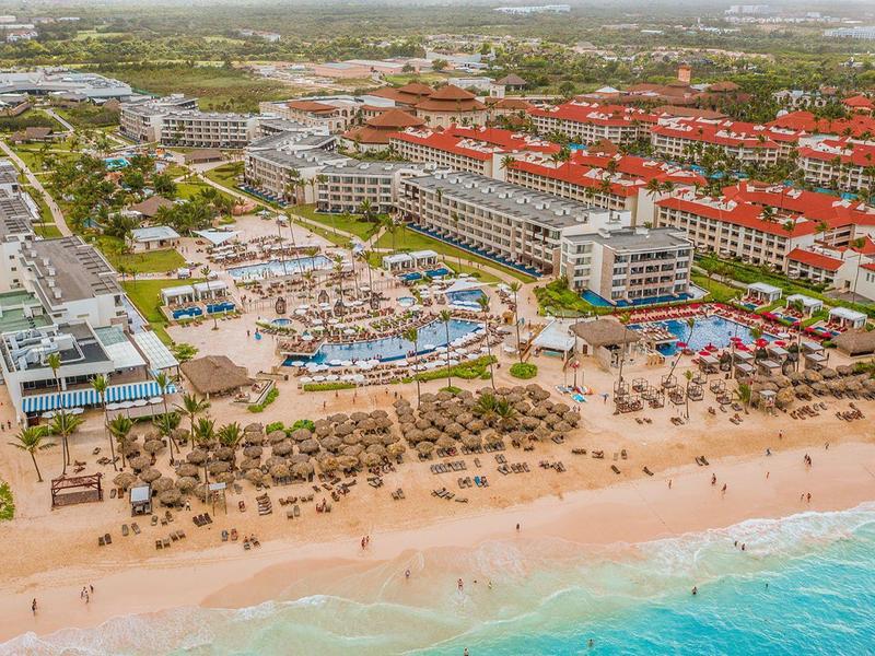 Velká pláž s hotely, bazény a lehátky podél pobřeží za slunečného dne.