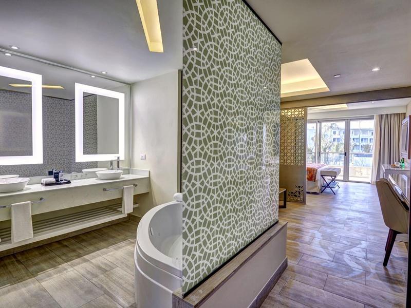 Moderní hotelová část s koupelnou, umyvadlem a přilehlým obývacím prostorem s velkým oknem.