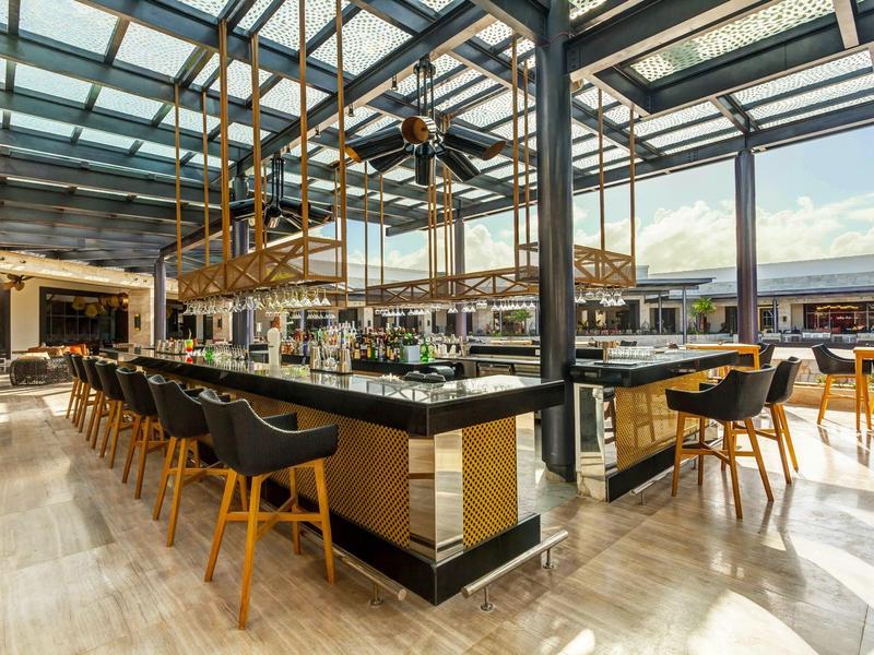 Moderní barová oblast s barovými židličkami a velkými okny, která propouštějí spoustu denního světla.