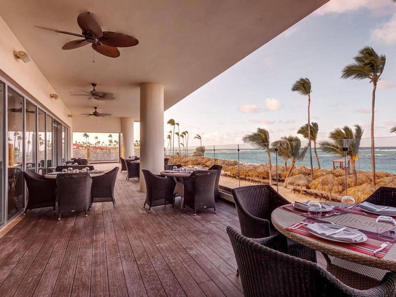 Terasa s prostřenými stoly a výhledem na moře při západu slunce.