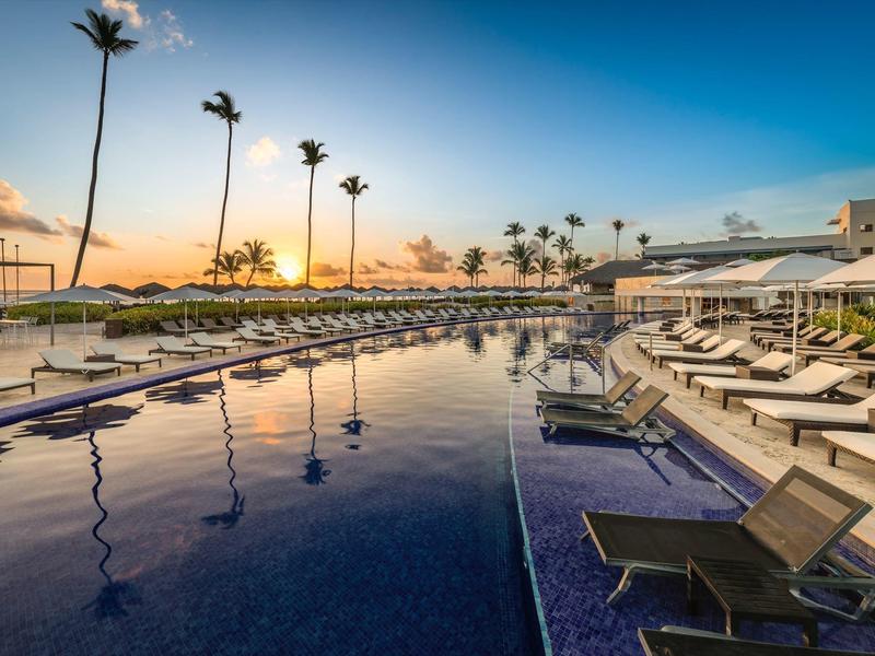 Moderní hotelový bazén s lehátky a palmami při západu slunce.