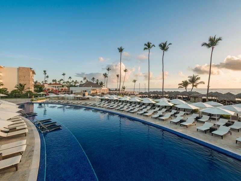 Moderní hotelový bazén s lehátky a palmami pod jasnou oblohou u moře.