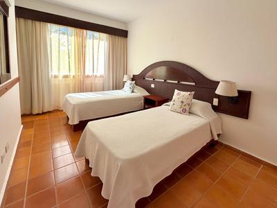 Bright hotel room with two single beds, brown headboard, and terracotta floor.