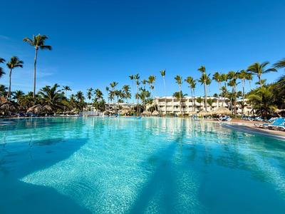 Large outdoor pool with palm trees and lounge chairs under a clear blue sky