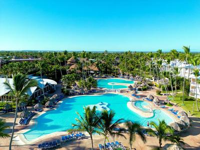 Large tropical hotel pool with palm trees and loungers under a clear blue sky