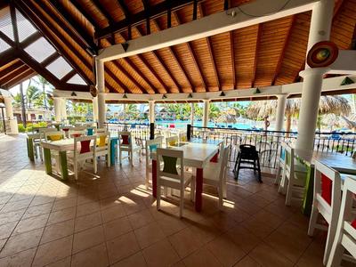 Covered dining area with colorful chairs and tables next to a pool in a hotel setting.