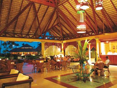 Open tropical hotel lobby with wooden ceiling, seating areas, and evening sky view