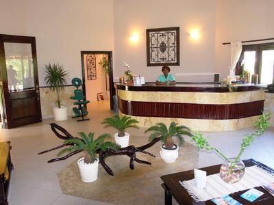 Bright hotel lobby with dark reception desk and plant arrangements on a carpet.
