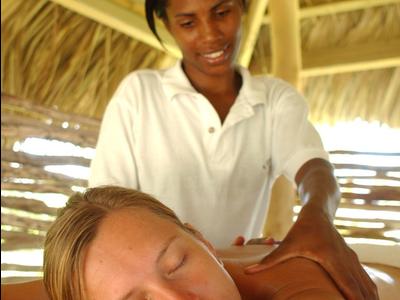 A woman receives an outdoor massage under a thatched roof.
