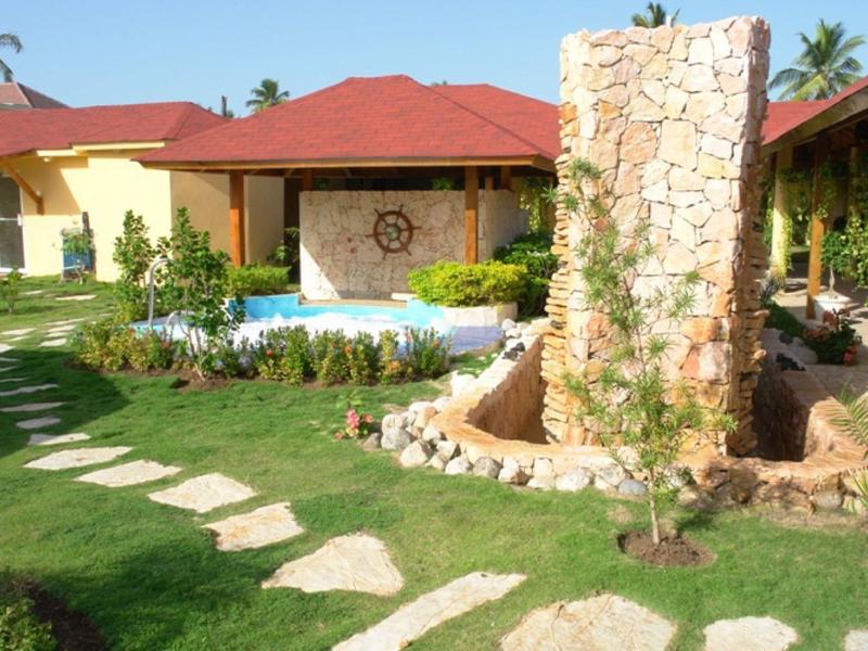 Hotel garden with pool, stone path, and large stone fountain under blue sky.