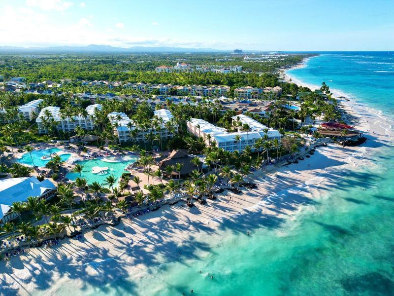 Aerial view of a beach resort with multiple pools, palm trees, and clear turquoise sea.
